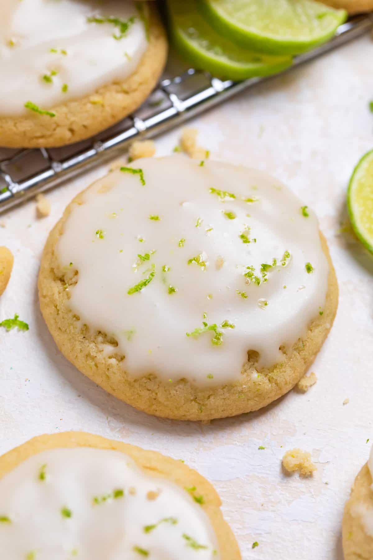 Key lime cookie with lime glaze on counter with other cookies and limes surrounding.