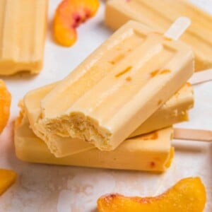 Creamy peach popsicles stacked with bite taken out of top popsicle.