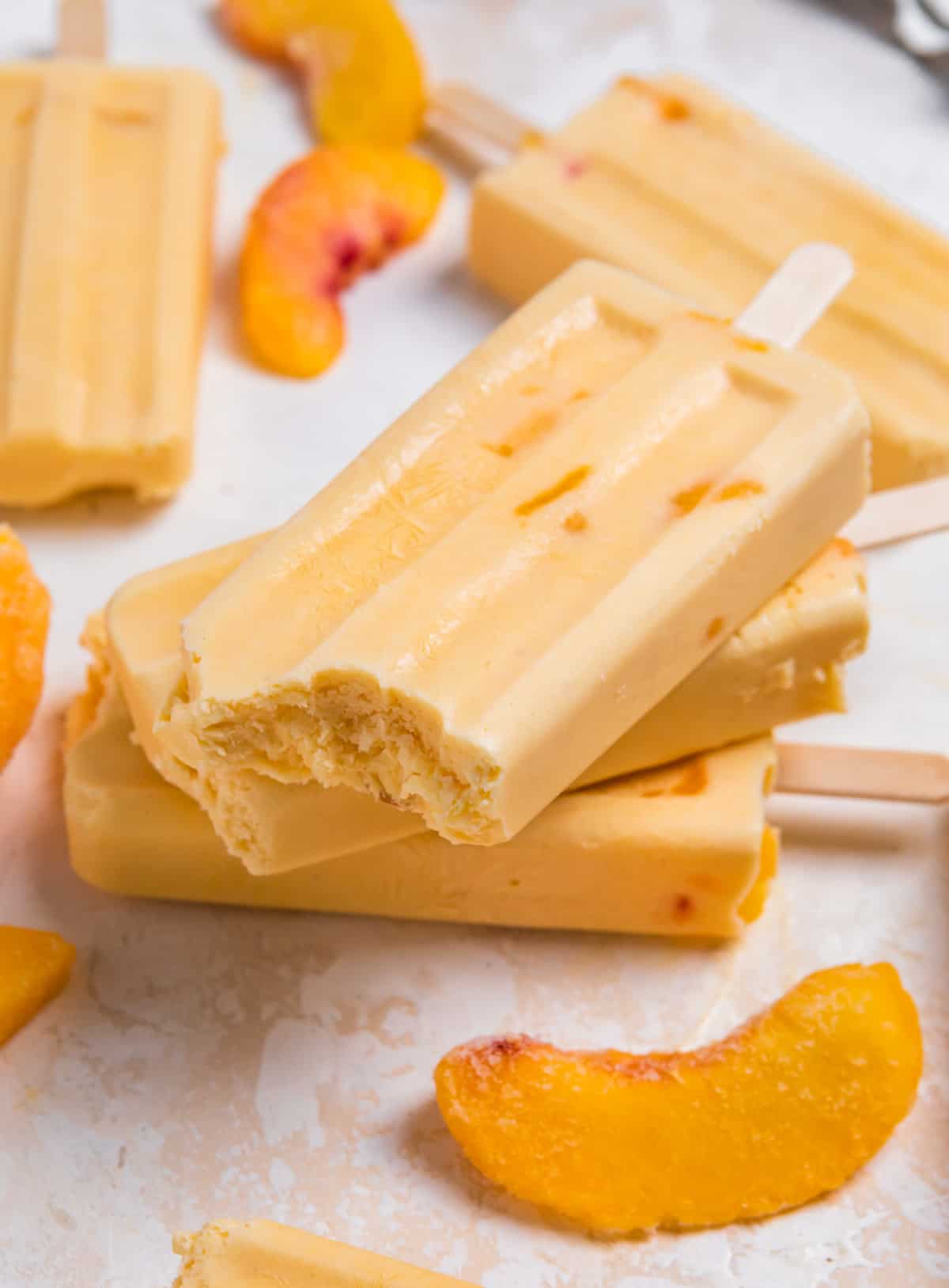 Stacked creamy peach popsicles with bite taken out of top popsicle.