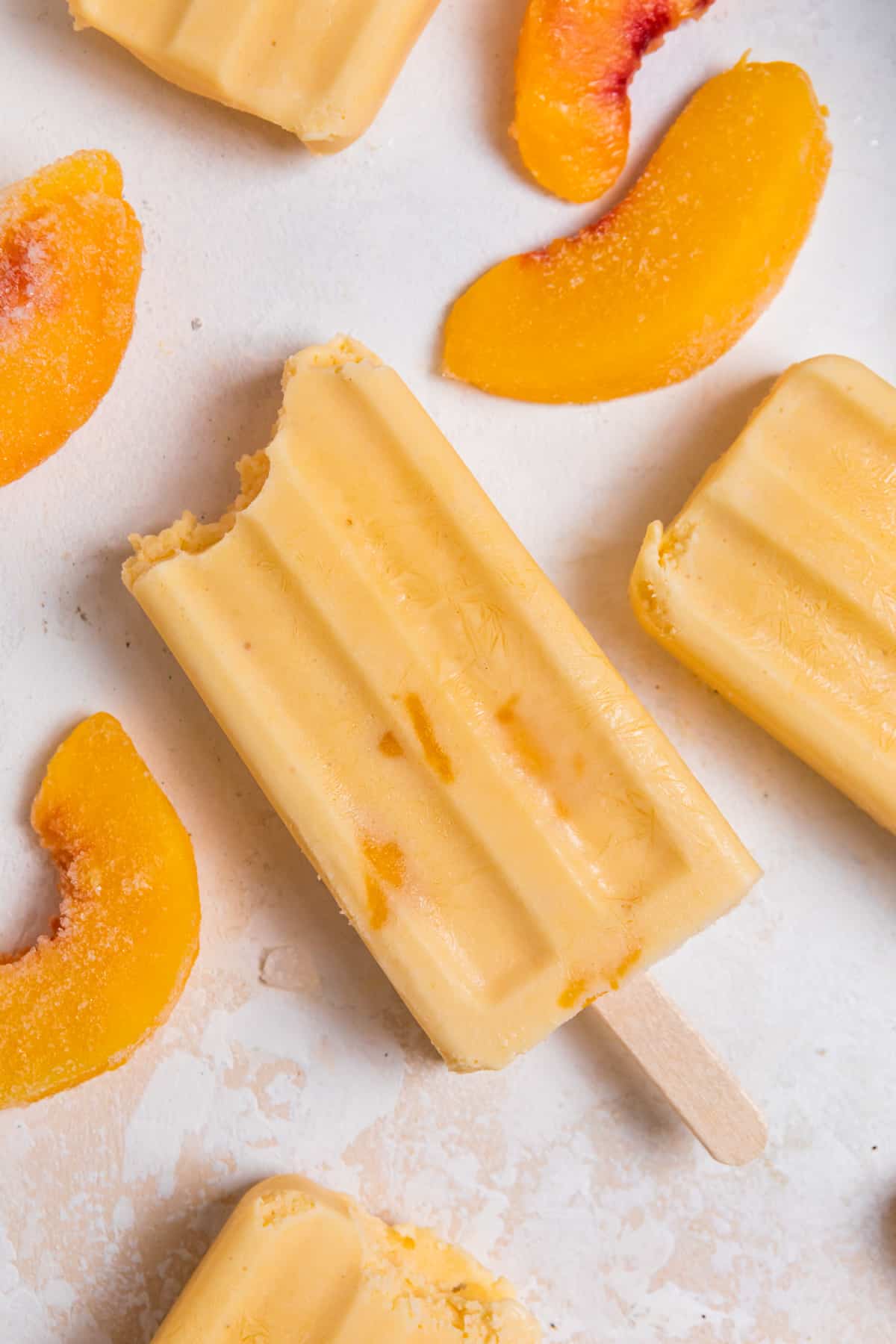 Peach popsicle on counter with peach slices surrounding.