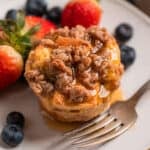 Baked French toast muffin with streusel topping on plate with maple syrup poured over top.