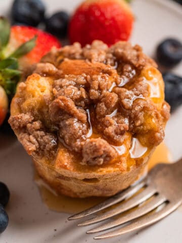 Baked French toast muffin with streusel topping on plate with maple syrup poured over top.