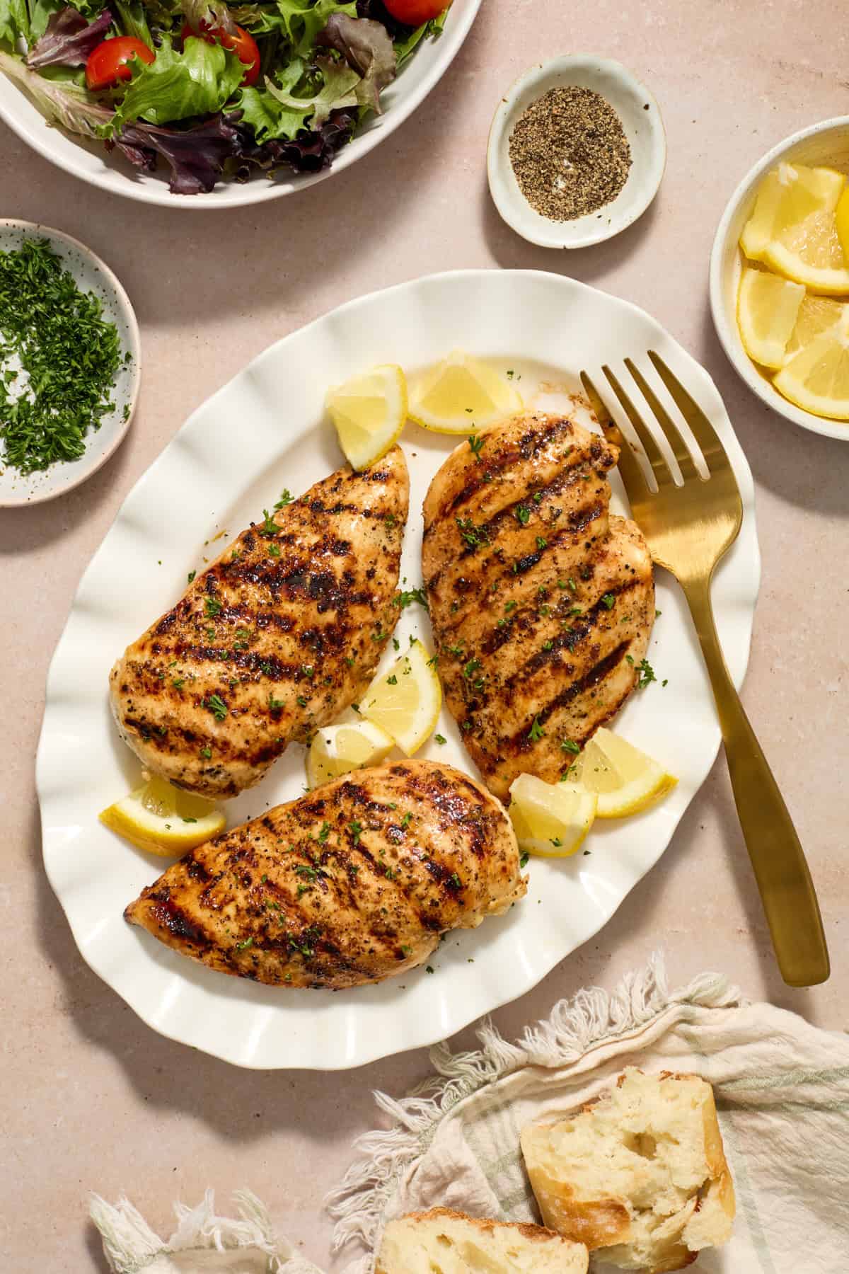 Lemon pepper grilled chicken breasts on plate with serving fork and lemons.
