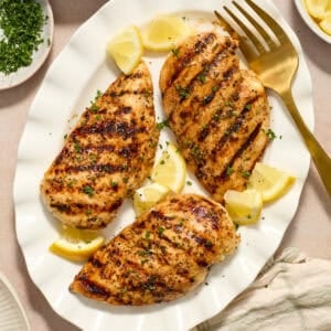 Grilled lemon pepper chicken on white serving platter with lemon wedges.