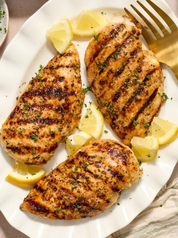 Grilled lemon pepper chicken on white serving platter with lemon wedges.