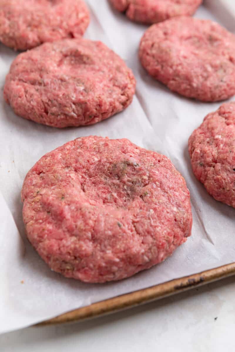 Burger patties prepared on pan with thumbprint in each.