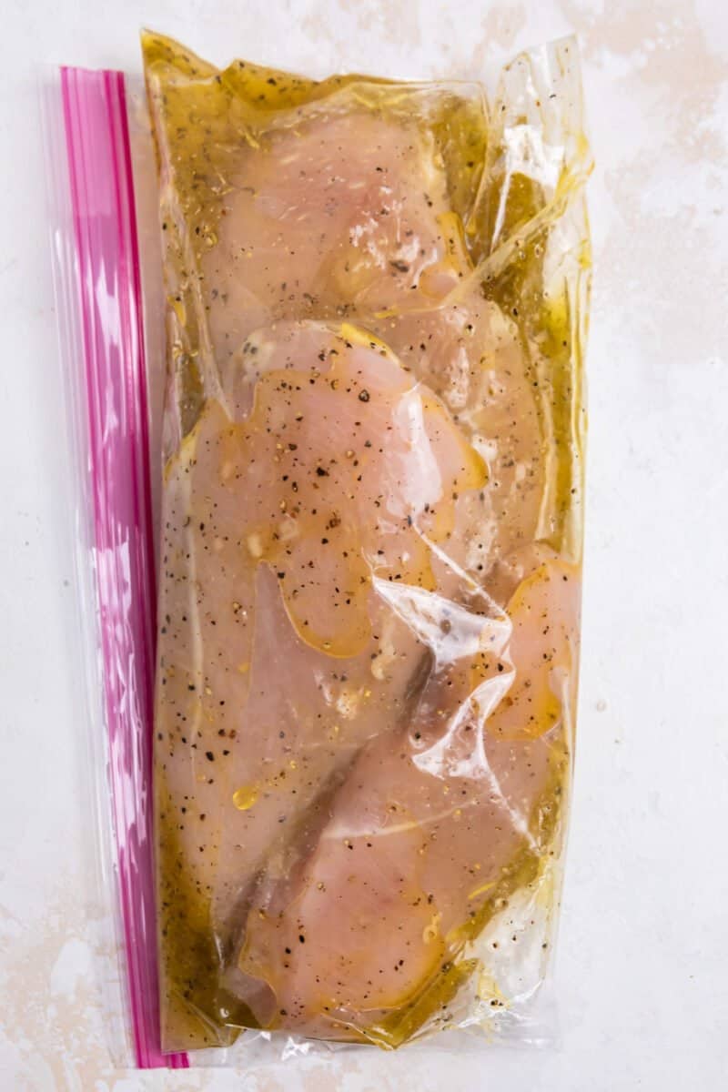 Chicken marinating in lemon pepper marinade in plastic bag.