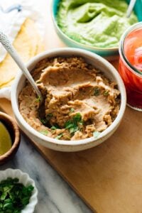Refried beans in bowl with spoon and other dishes surrounding.