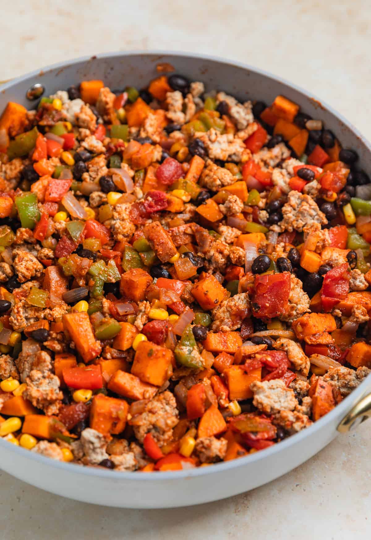 Turkey and pepper mixture stirred into sweet potato, bean, corn mixture in skillet.