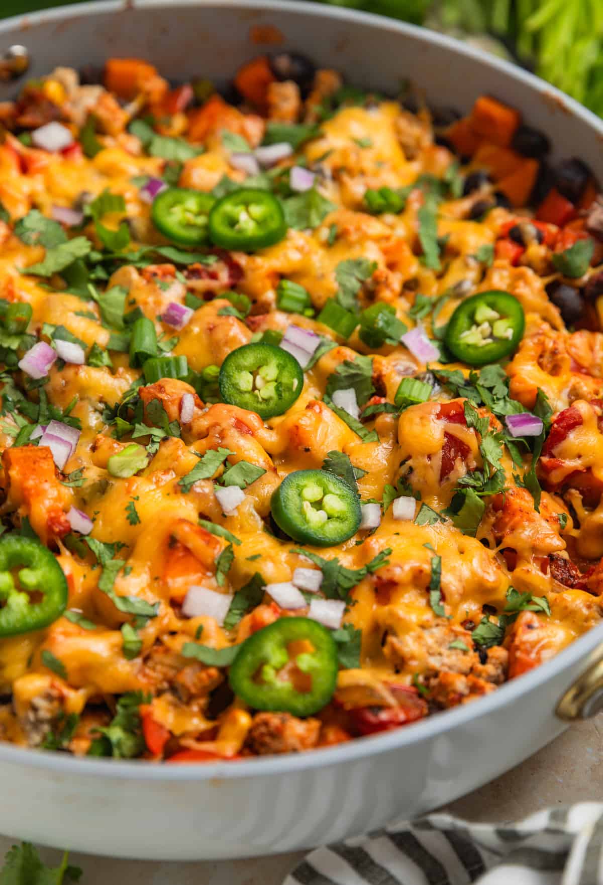 Skillet with cooked meat and vegetables topped with melted cheese, cilantro, peppers, onions and more.
