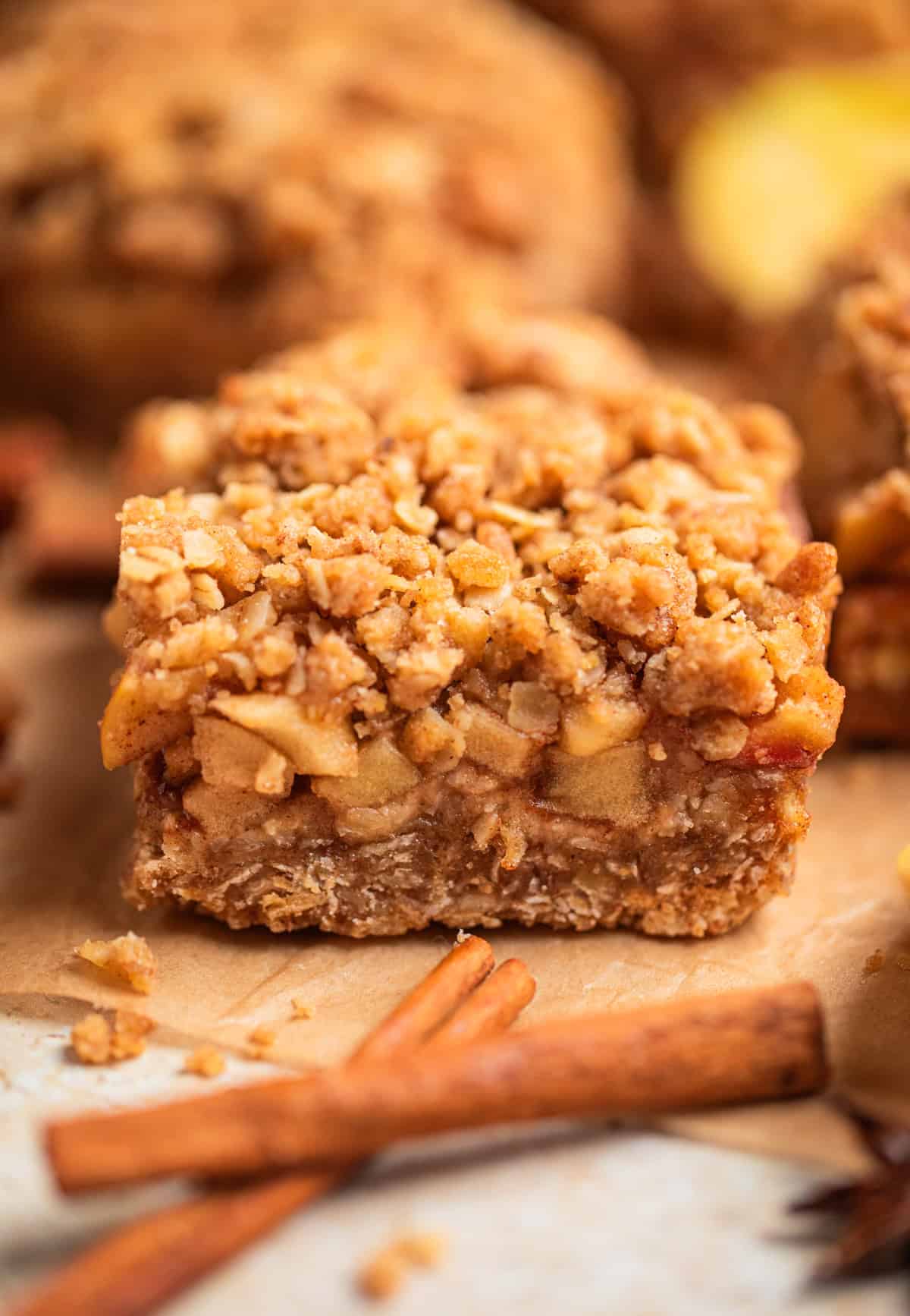 Apple pie crumb bars on parchment with cinnamon sticks.