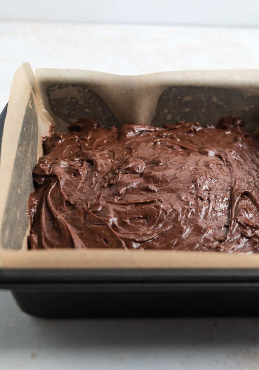 Brownie batter in 8 inch square baking pan lined with parchment paper.