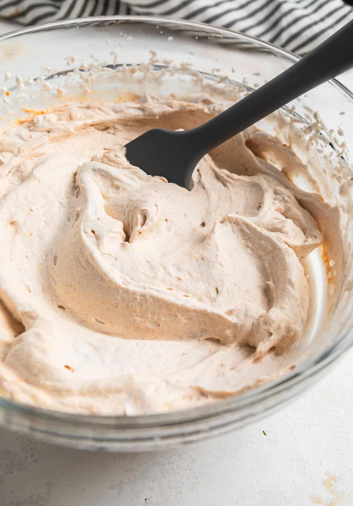 Pumpkin spice whipped cream in mixing bowl with spatula.