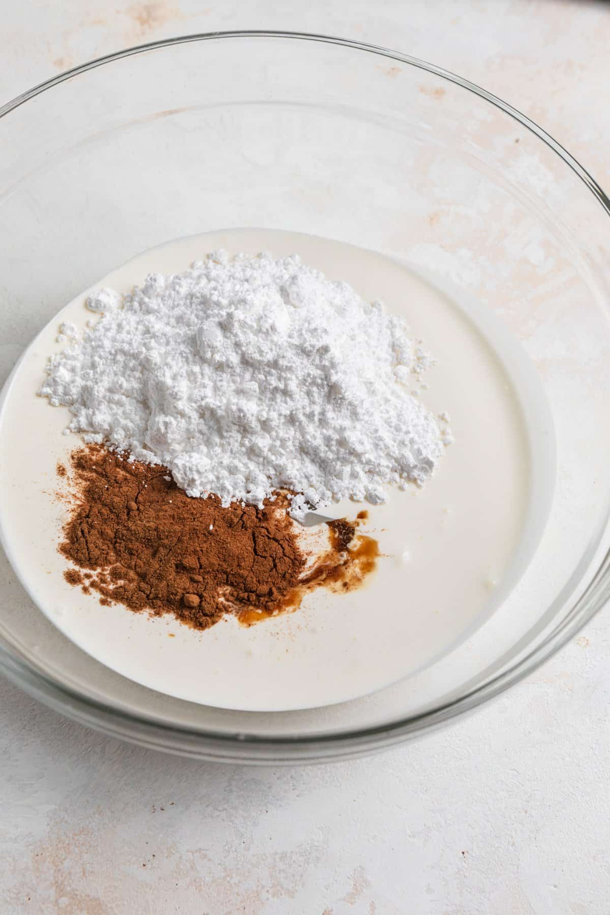 Heavy cream, cinnamon, powdered sugar and vanilla in glass mixing bowl.