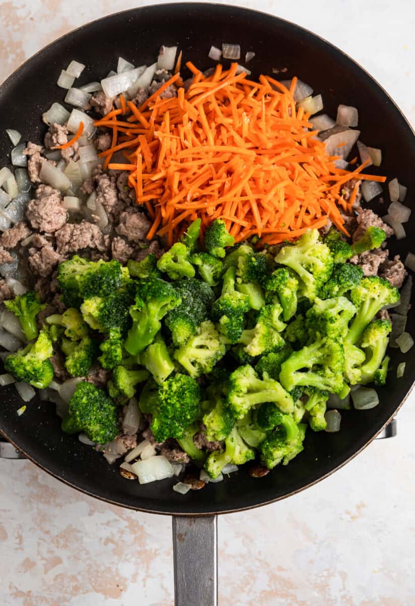 Frozen broccoli and shredded carrots added over top meat and onion mixture in skillet.