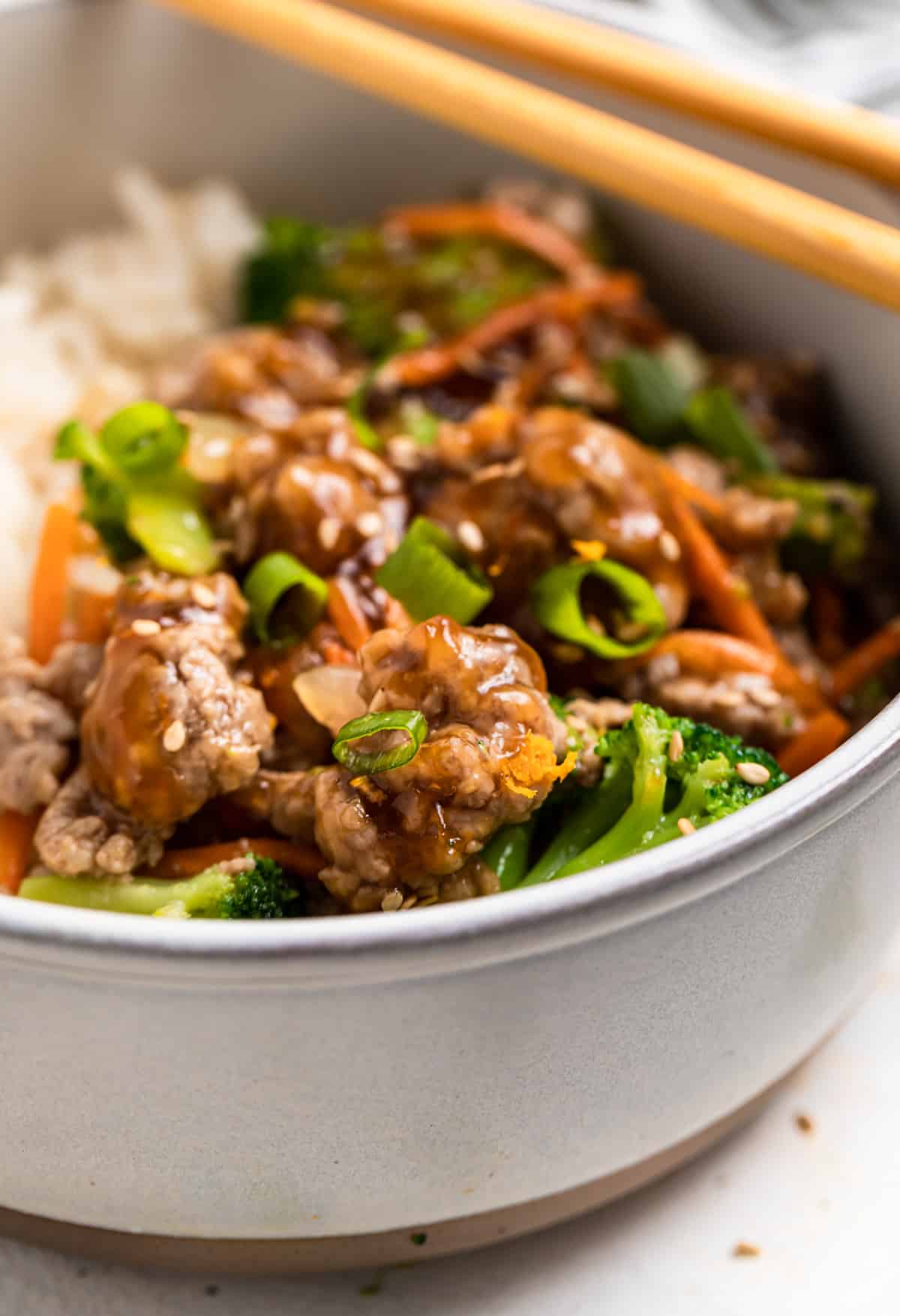 Bowl with ground pork teriyaki stir fry topped with sesame seeds and chopsticks on top of bowl.