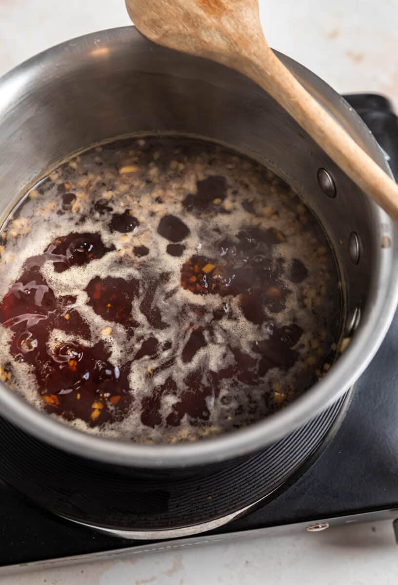 Teriyaki sauce boiling in sauce pan with wooden spoon set on top.