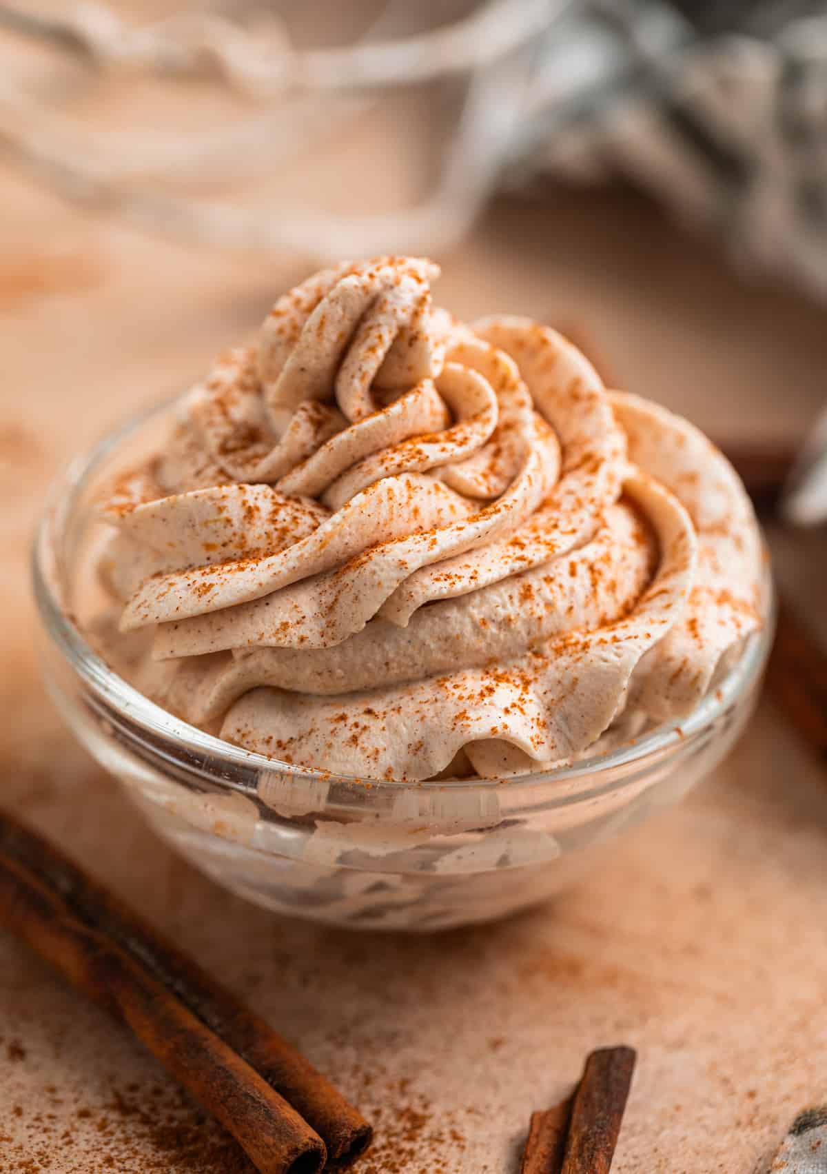 Pumpkin spice whipped cream piped into glass bowl with cinnamon dusted on top and cinnamon sticks beside it.