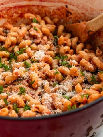 Red dutch oven with creamy one pot pasta topped with parsley and parmesan.