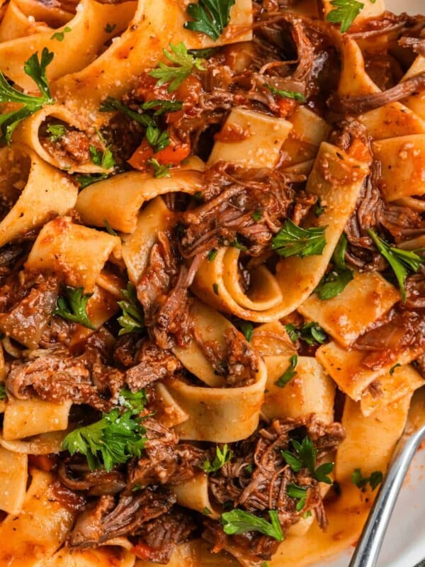 White plate with short rib ragu tossed with pappardelle pasta and topped with parsley.