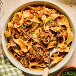 Bowl with short rib ragu tossed with pasta and chopped fresh parsley over top.