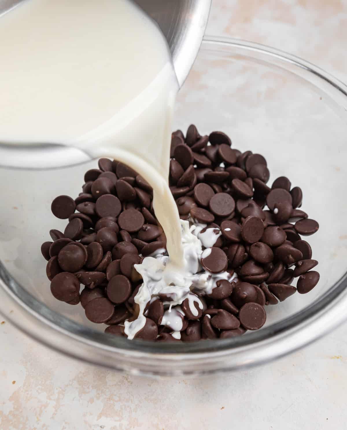 Heavy cream poured into chocolate chips in glass mixing bowl.