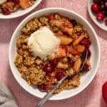 Bowl with cranapple crisp with vanilla ice cream and spoon propped in the bowl.