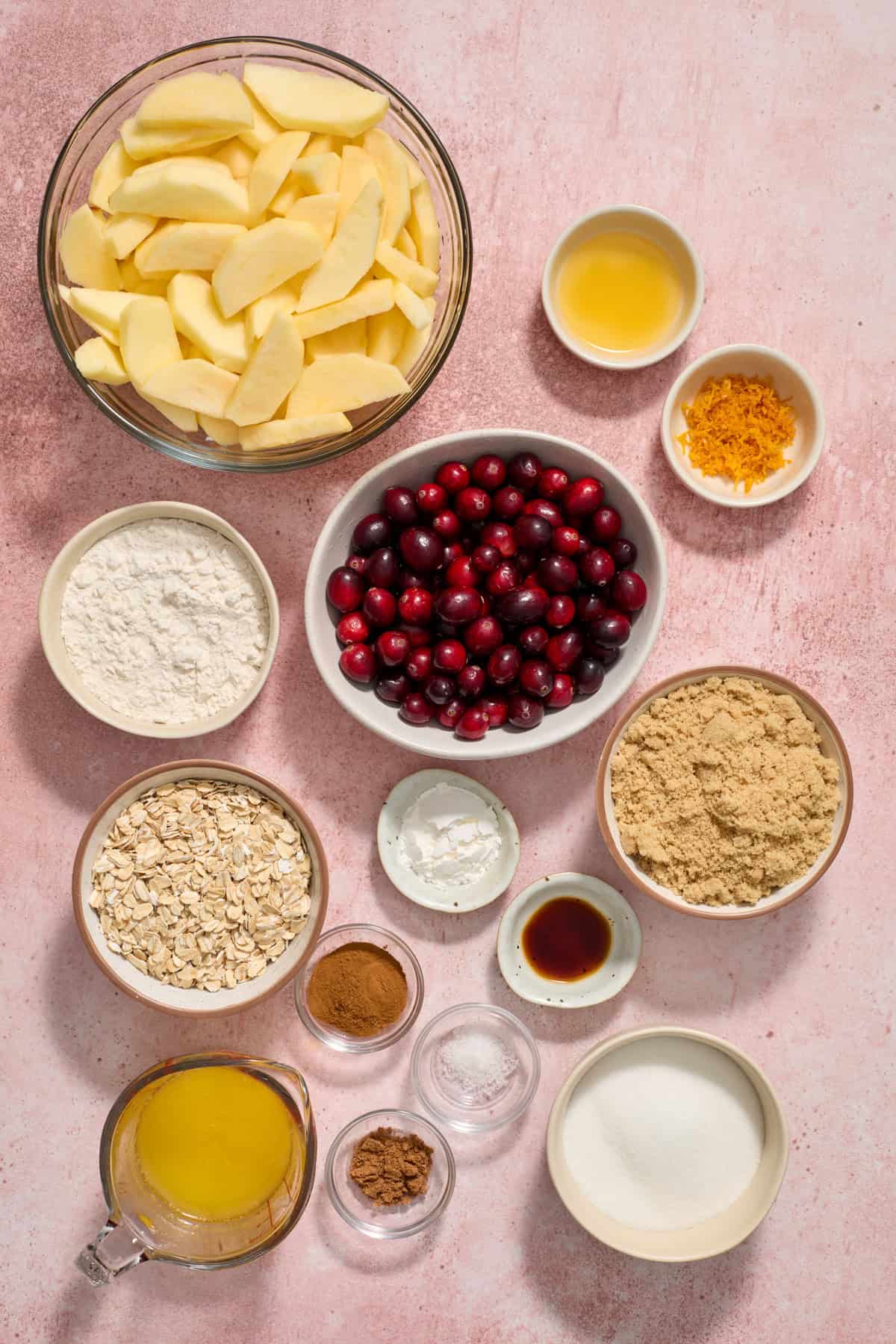 Sliced apples, orange zest, flour, butter, sugar and more arranged on surface.
