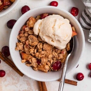 Bowl with apple cranberry crisp topped with vanilla ice cream.