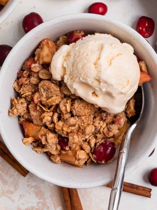 Bowl with apple cranberry crisp topped with vanilla ice cream.