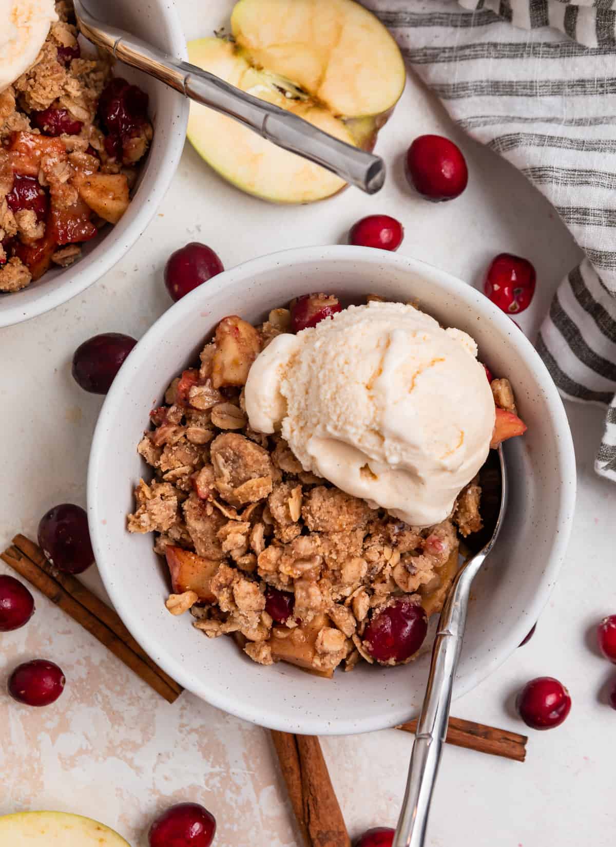 Apple cranberry crisp in white bowl with scoop of vanilla ice cream and spoon.