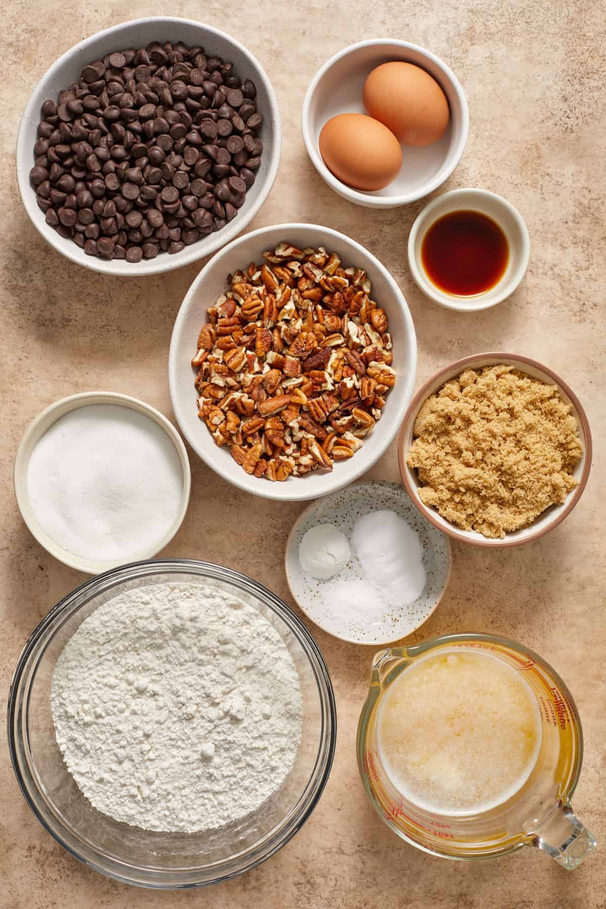 Butter, eggs, flour, pecans, chocolate chips and other ingredients arranged on surface.