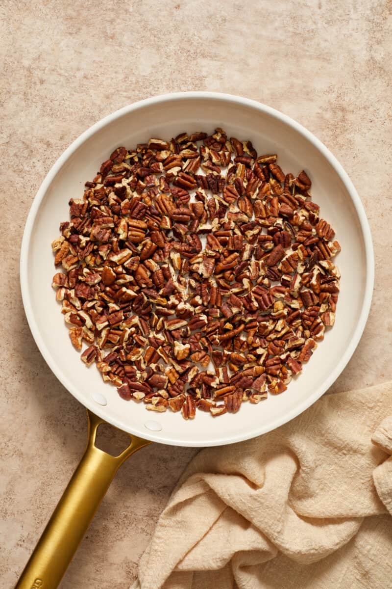 Chopped pecans in skillet with tan linen beside it.