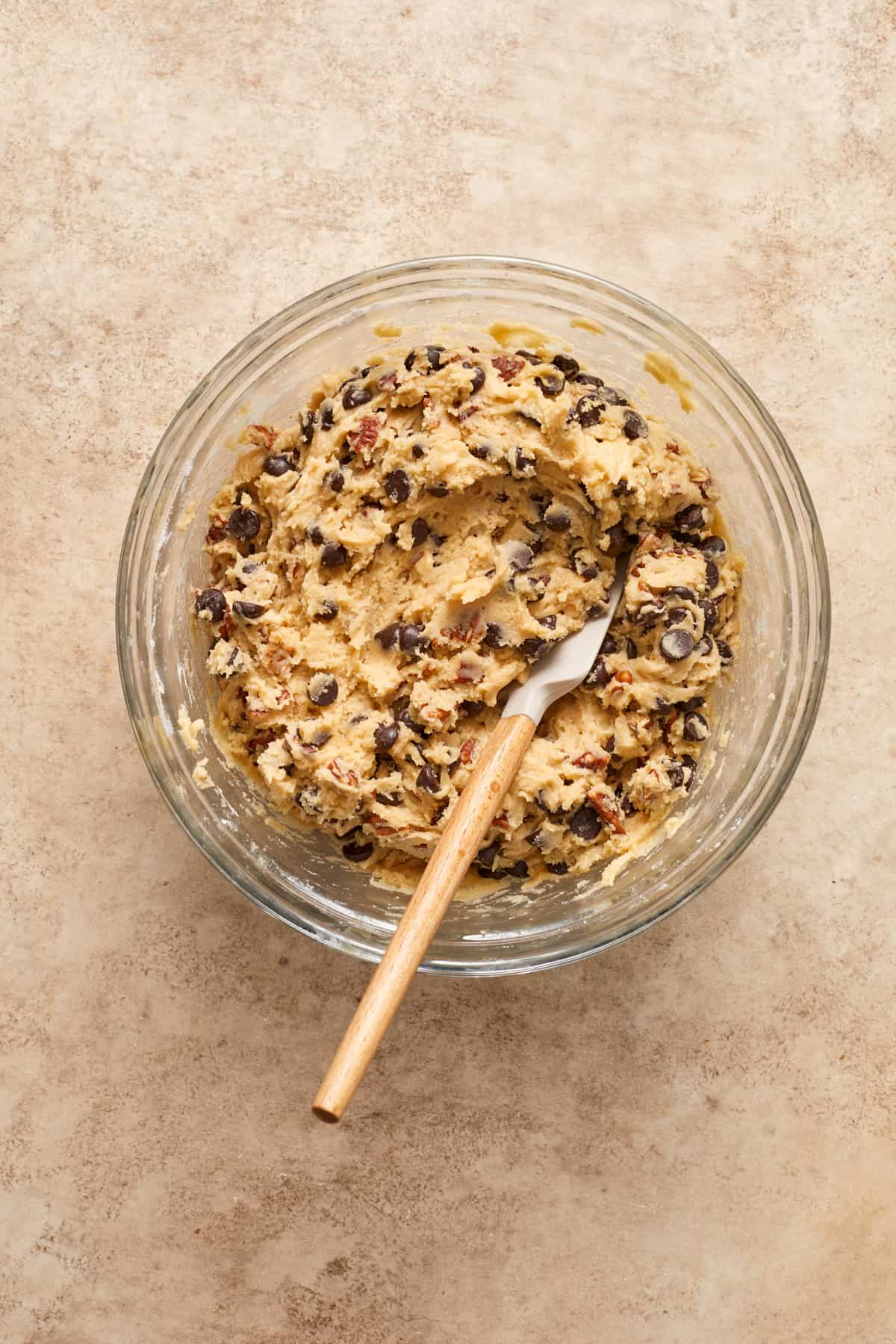 Chocolate chip pecan cookies dough in bowl with spatula.