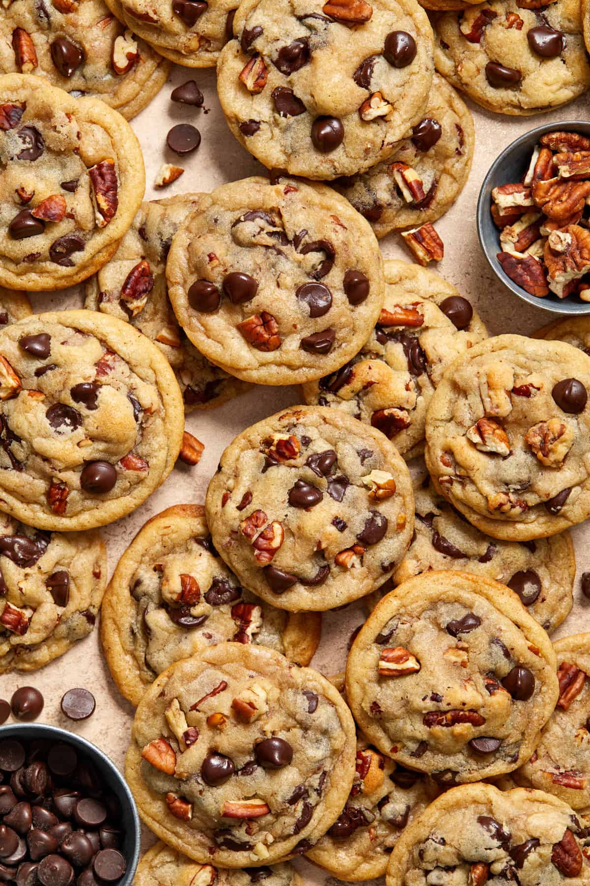 Chocolate chip cookies with pecans added along with bowl of chocolate chips and pecans beside.