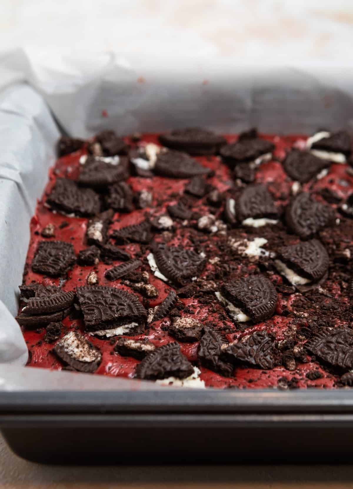 Oreo red velvet fudge in parchment lined pan and topped with crushed Oreos.