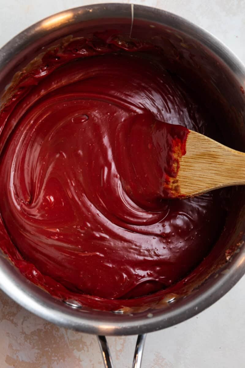 Red velvet fuge prepped in sauce pan with wooden spoon.