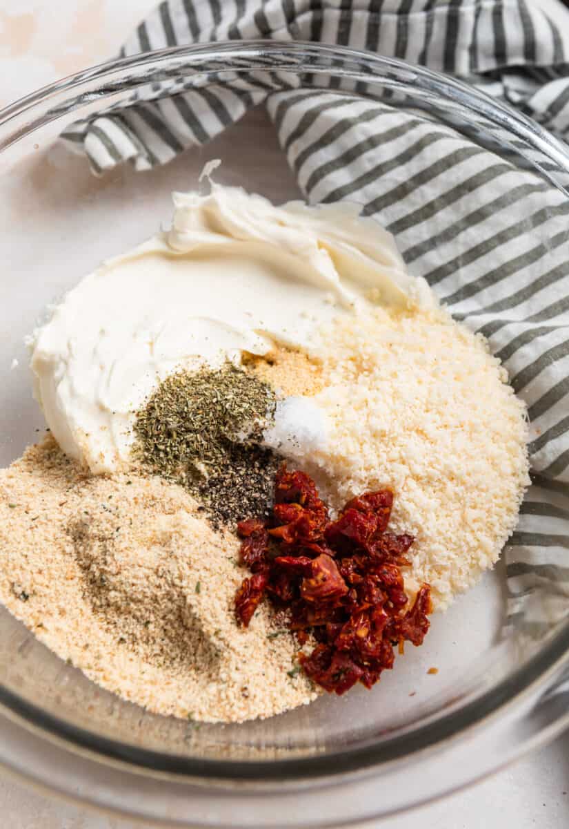 Cream cheese, parmesan, sun-dried tomatoes, and other ingredients in glass mixing bowl.