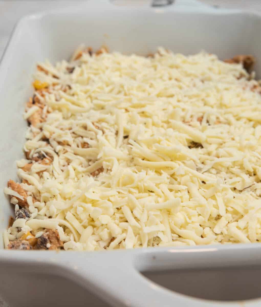 Chicken taco casserole topped with shredded cheese in white casserole dish.