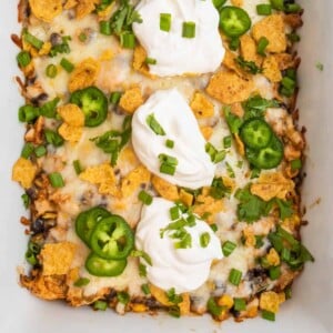 Chicken taco casserole in white dish topped with sour cream, green onions and other toppings.