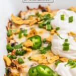 Chicken taco casserole in white dish with cilantro, sour cream and chips on top.