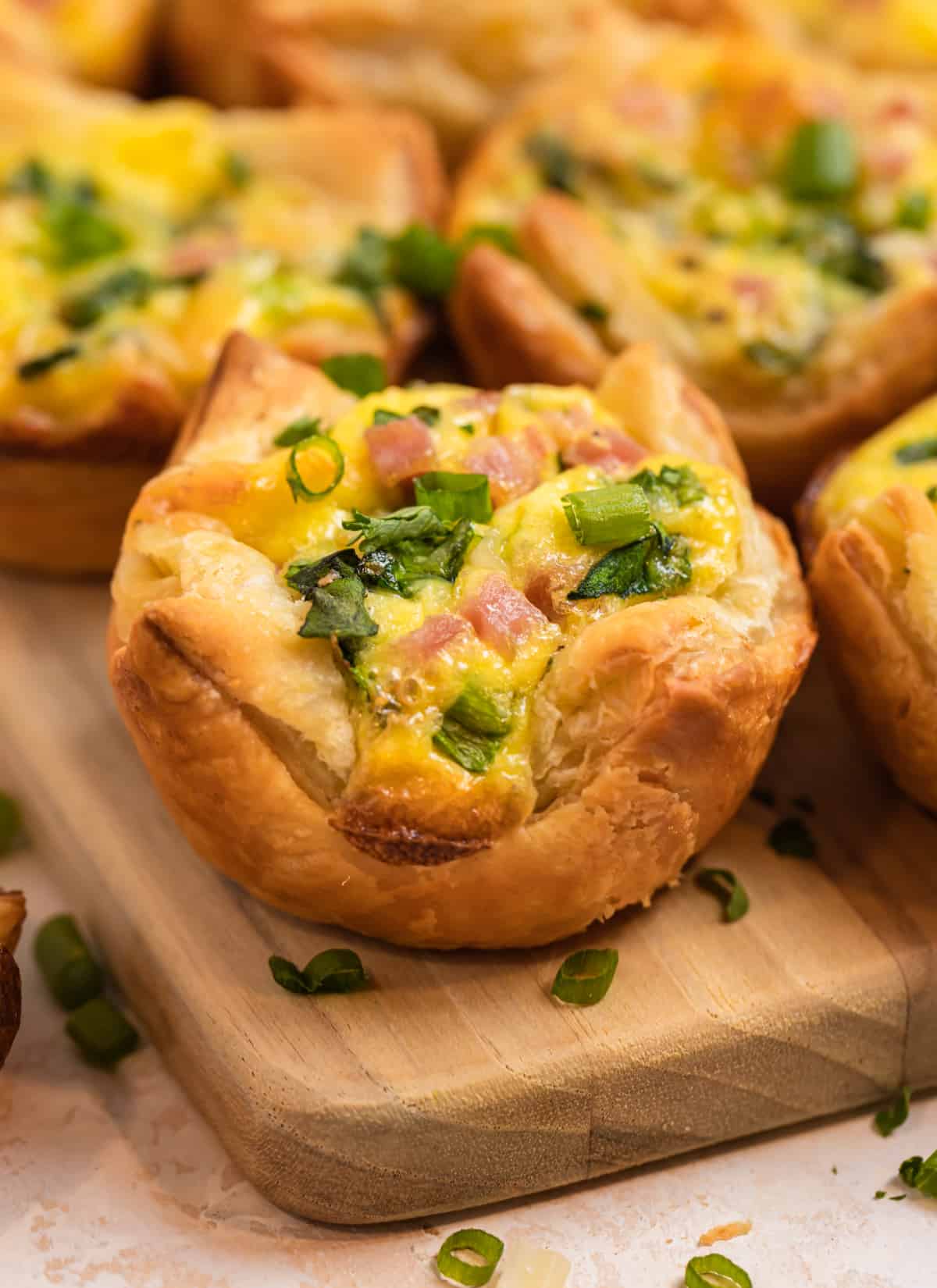 Puff pastry mini quiches with ham and spinach on wood platter topped with green onion and parsley.