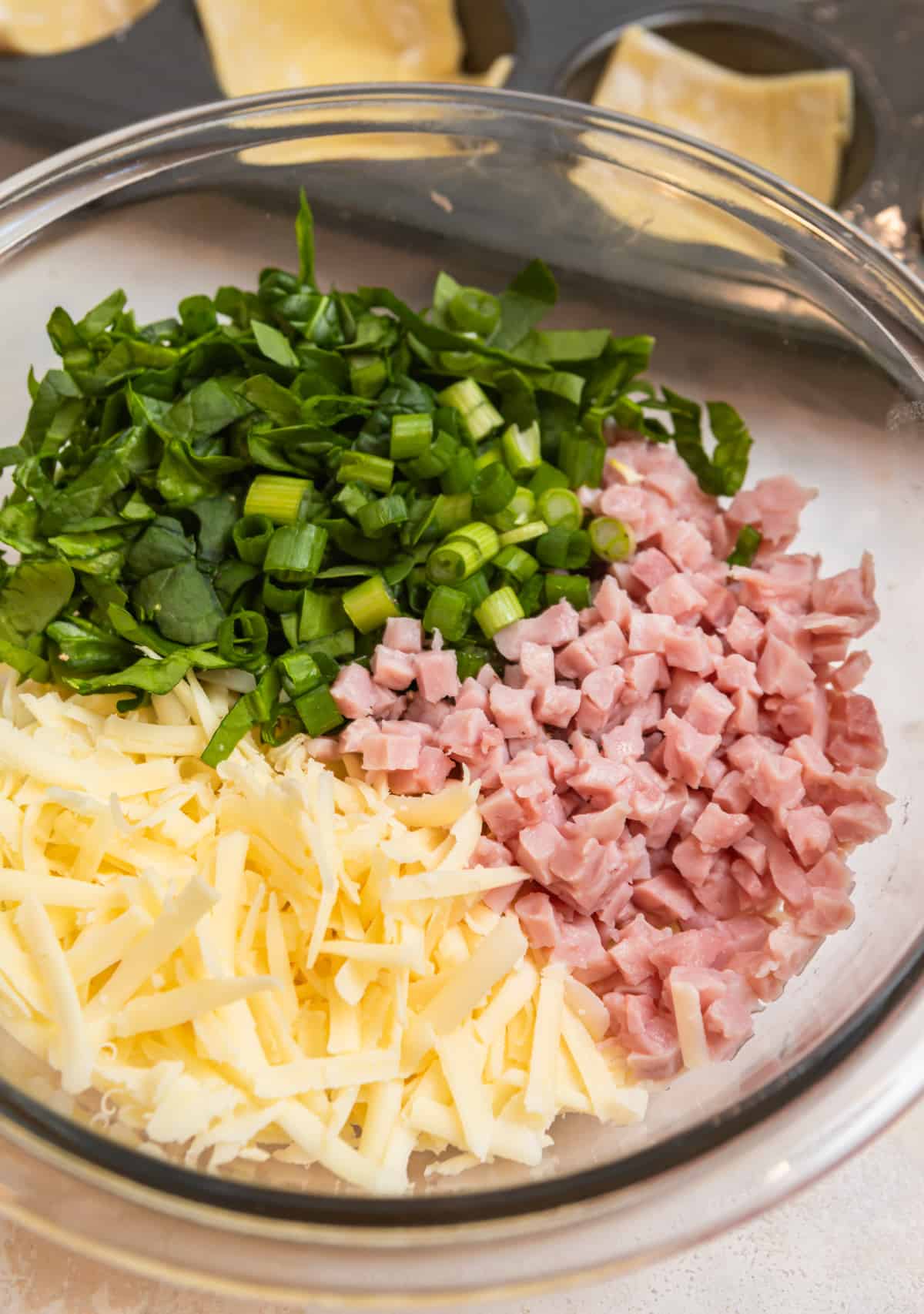 Ham, cheese, onion, and spinach in glass mixing bowl.