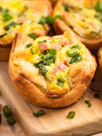Mini quiches with puff pastry on wood board topped with onion and chopped parsley.