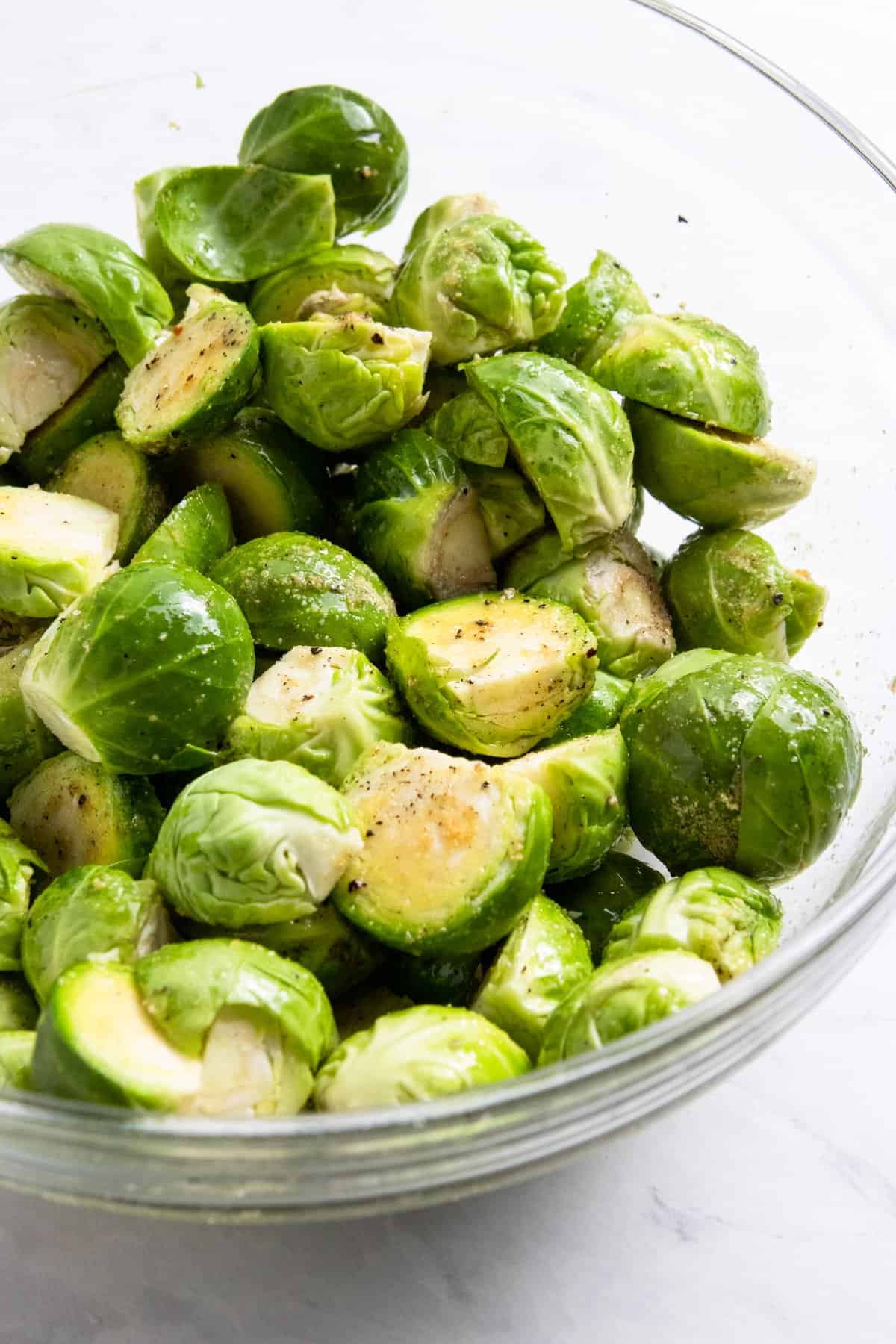 Glass bowl with brussels sprouts tossed in olive oil and seasonings.