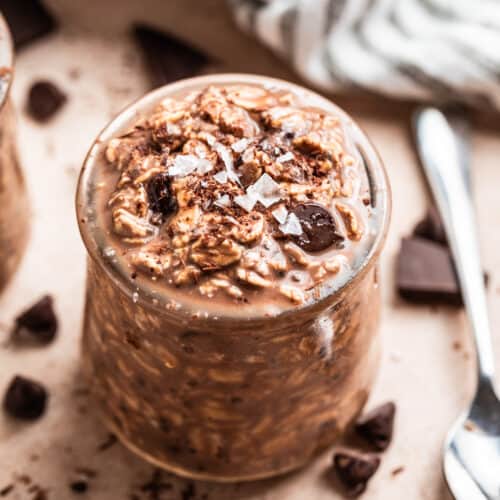 Chocolate overnight oatmeal in jar with spoon and chocolate pieces beside it.