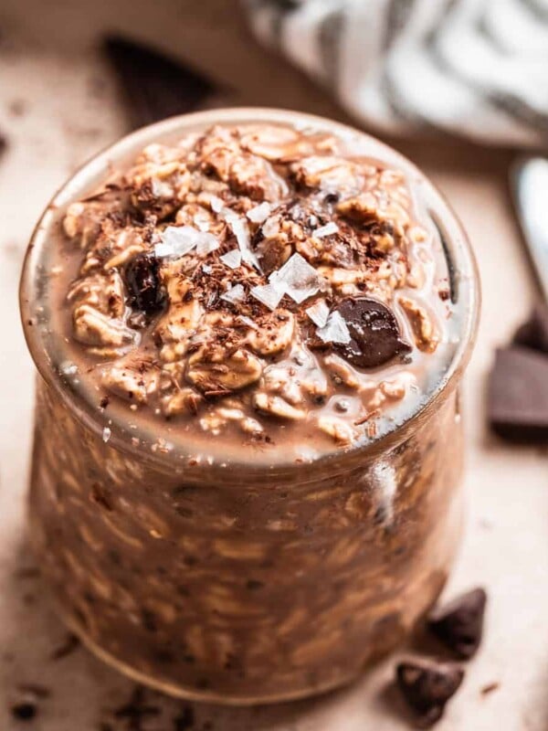 Chocolate overnight oatmeal in jar with spoon and chocolate pieces beside it.