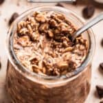 Chocolate oatmeal in glass jar with spoon dipping into it.
