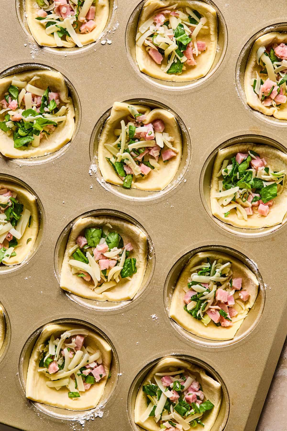 Puff pastry squares in muffin tin filled with ham, cheese and spinach.