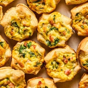 Mini quiches with puff pastry on plate topped with onion and chopped parsley.
